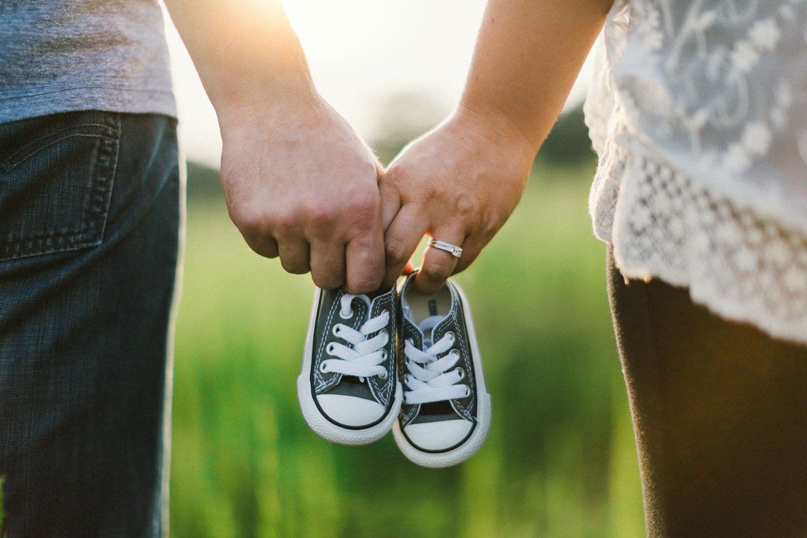 An expecting couple holding hands and a tiny pair of baby sneakers outdoors