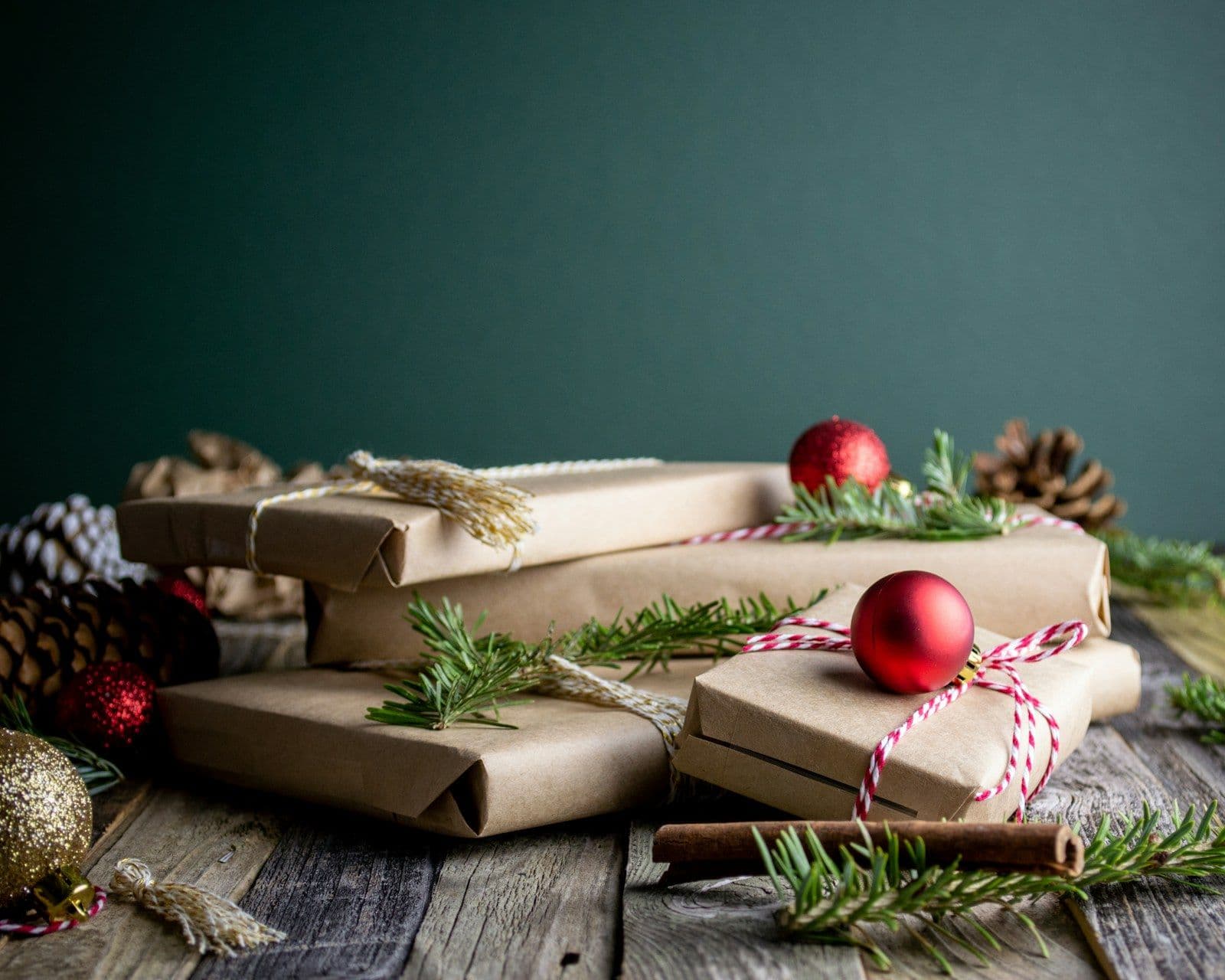 Gifts wrapped in plain brown paper with twine, pine sprigs and red ornaments on a wooden table